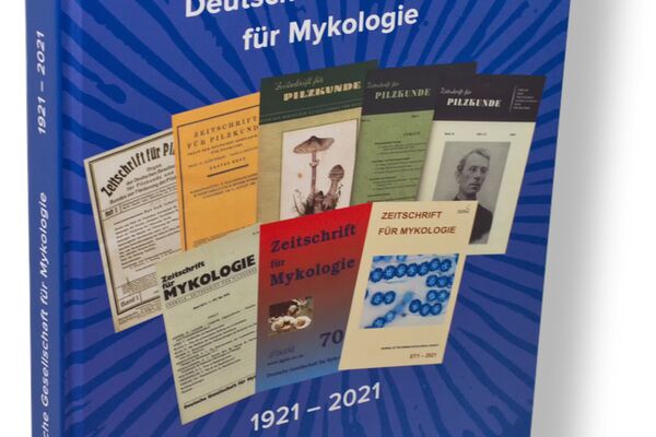 Titelseite des „Jubelbuchs“ mit Zeitschriften des zurückliegenden Jahrhunderts vor dem Sporenpulverabdruck eines Lamellenpilzes im Hintergrund